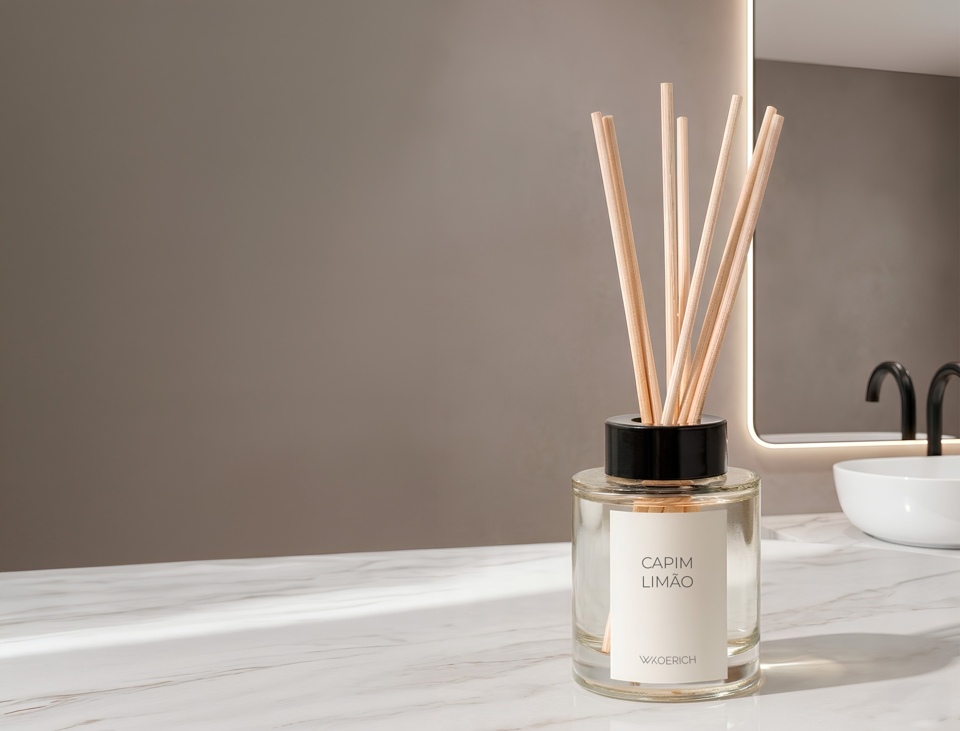 difusor-capim-limão-wkoerich-spa-particular.jpg Um difusor de ambientes em frasco de vidro transparente com varetas de madeira e rótulo branco escrito "CAPIM LIMÃO" e a logo "WKOERICH". O frasco está sobre uma bancada de mármore branco, com um espelho e pia de banheiro ao fundo.